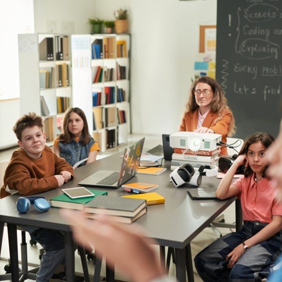Group of children with female teacher watching presentation in school classroom and using projector boy silhouette in foreground